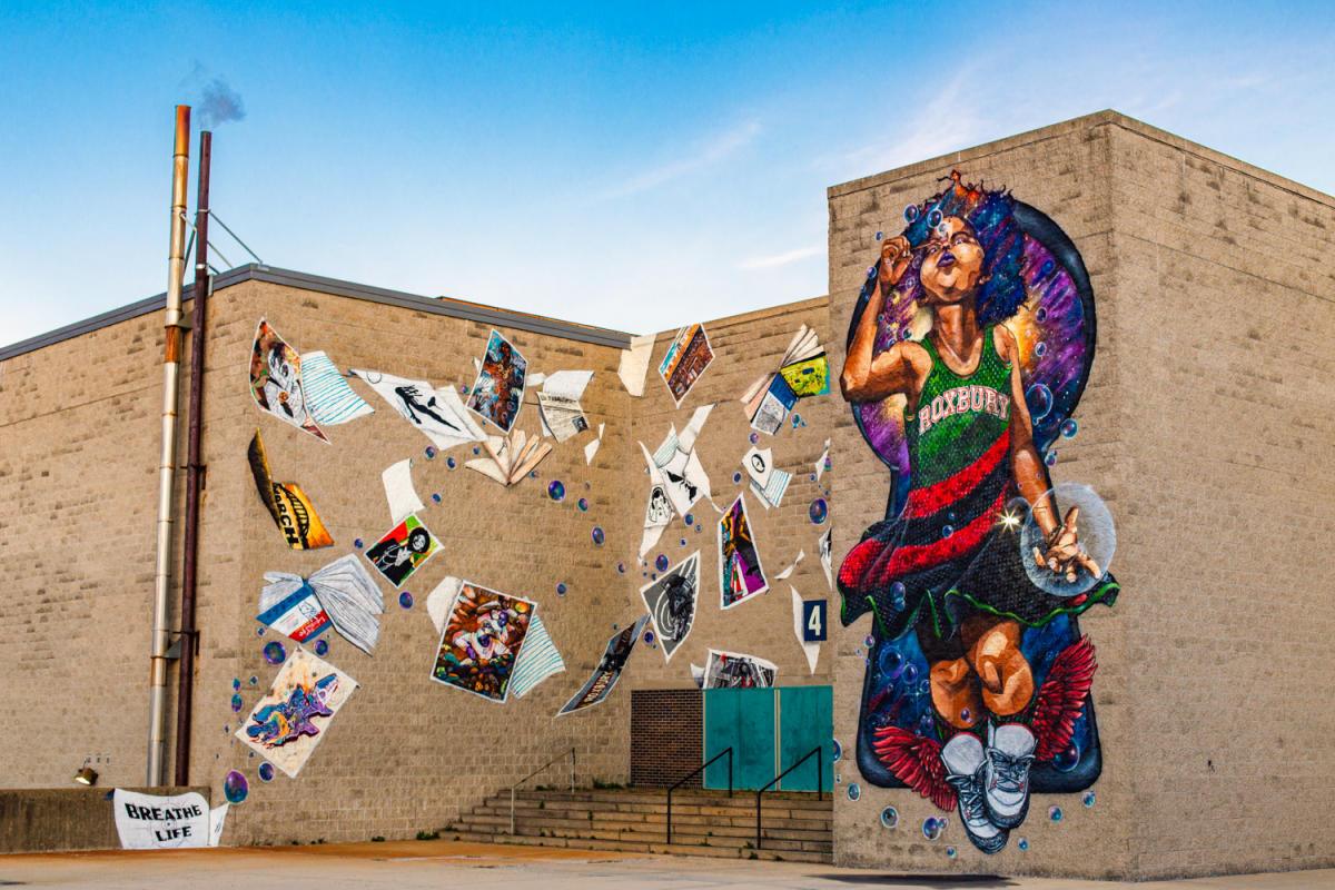 Colorful mural on side of building of girl blowing bubbles and books floating in the air.